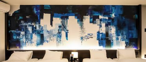 A hotel room with two beds, a large abstract painting on the wall, and a nightstand with a lamp and phone.