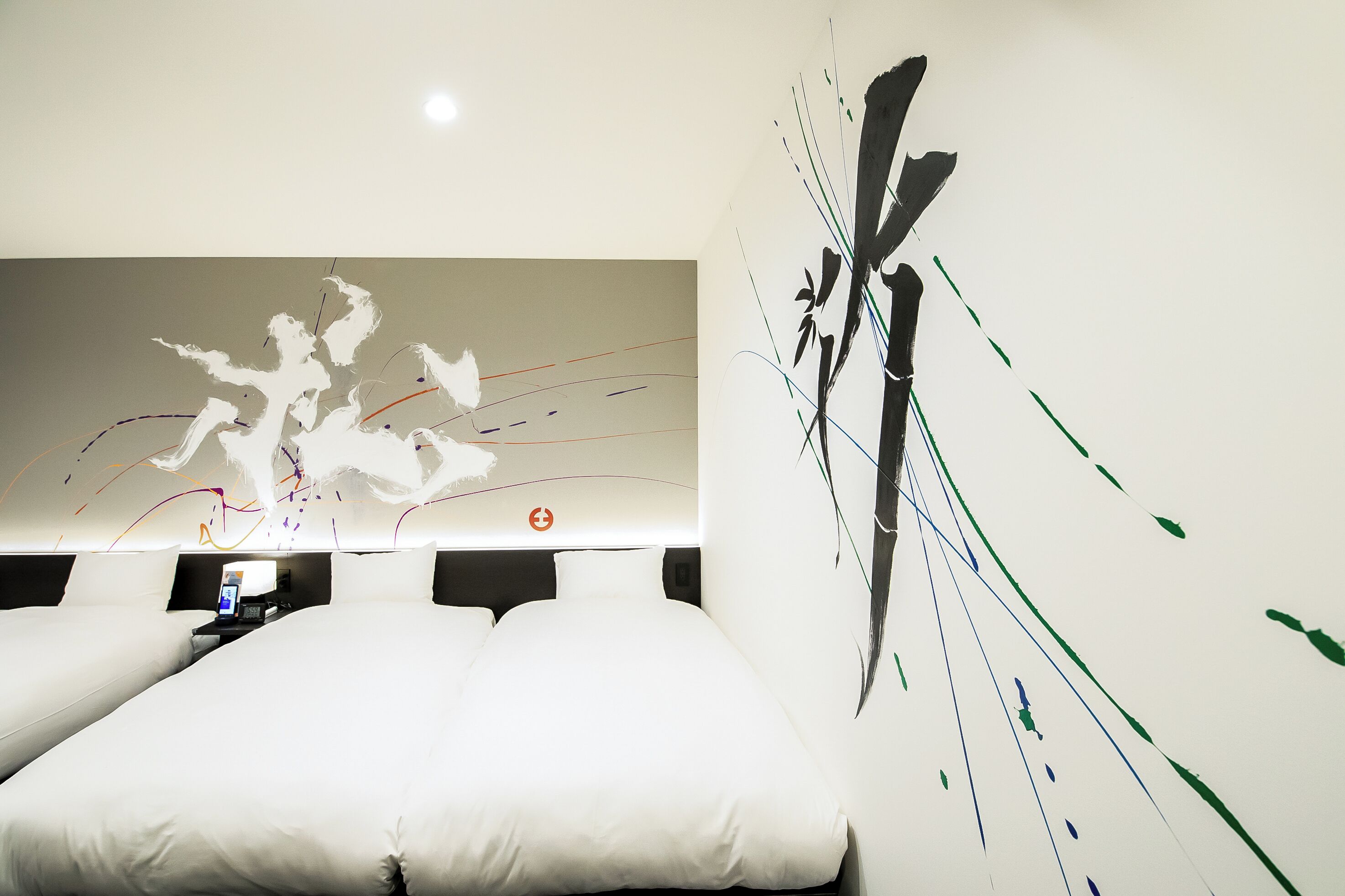 A hotel room with a large bed, a desk with a laptop, and a wall with abstract art.