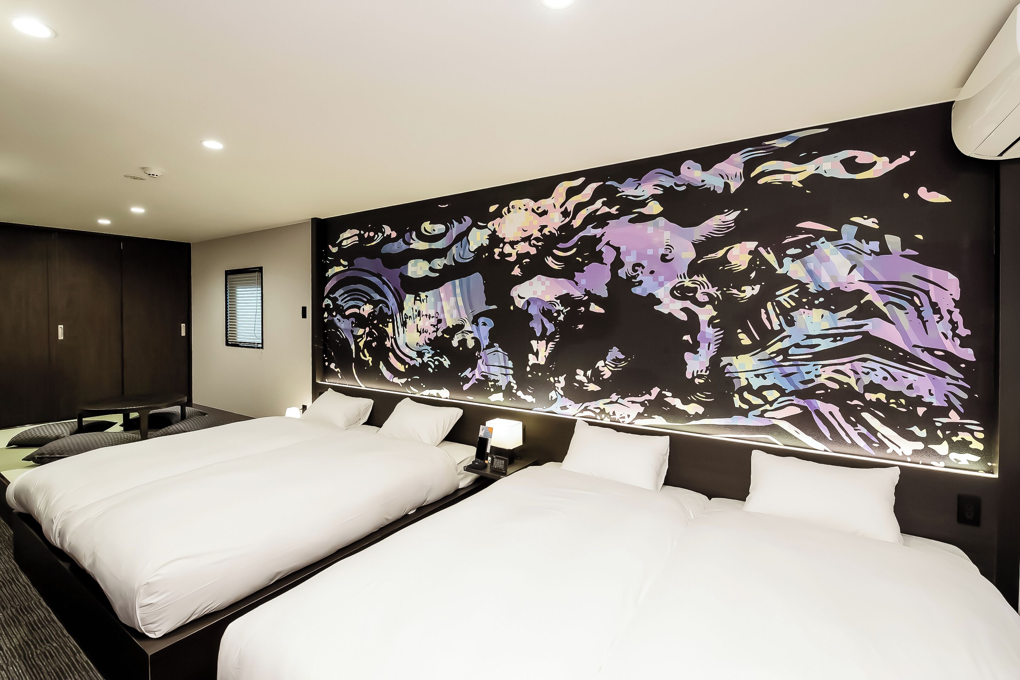 Habitación de hotel con dos camas, un mural abstracto grande en la pared y un diseño moderno.