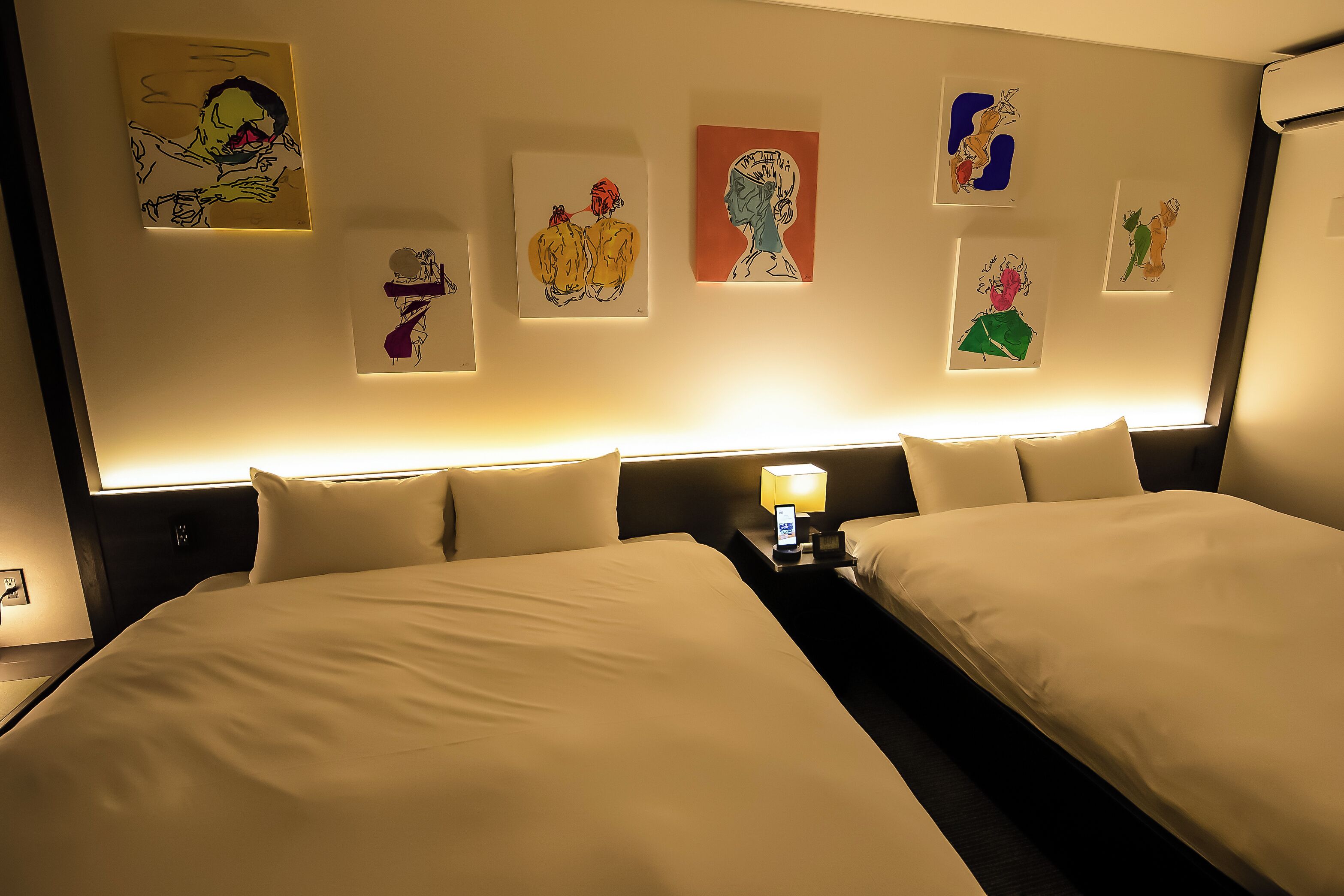 Een hotelkamer met twee bedden, een nachtkastje met een lamp en kunst aan de muur.