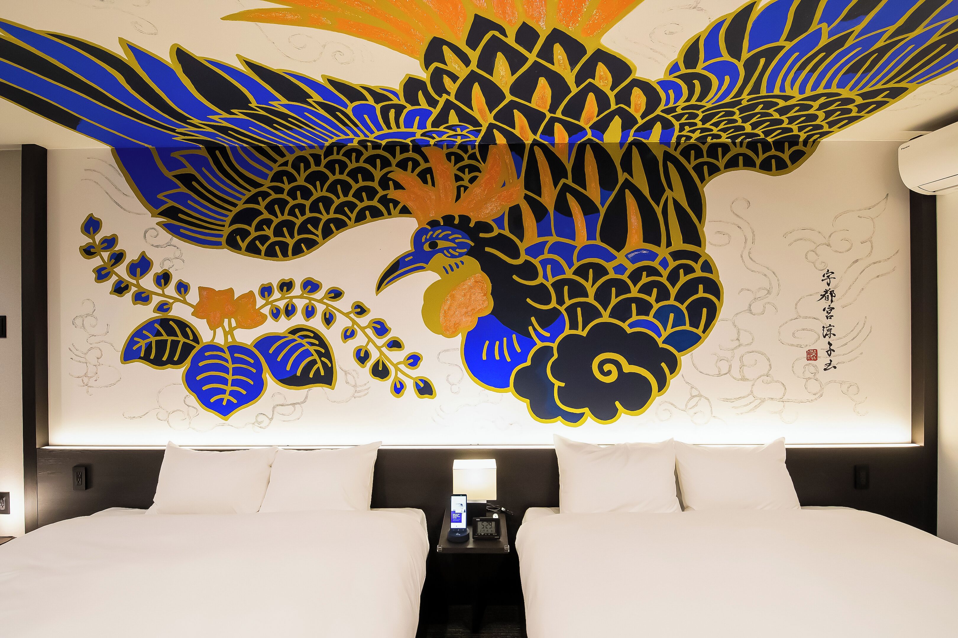 Ein Hotelzimmer mit einer großen Wandmalerei von einem Pfau, einem Bett und einem Nachttisch mit Telefon.