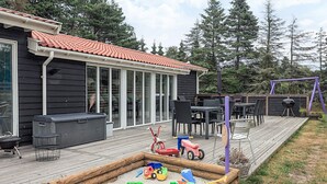 A wooden deck with outdoor furniture, a play area with toys, and a barbecue grill. - 4 Star Holiday Home in Vaeggerlose (Vaeggerlose)