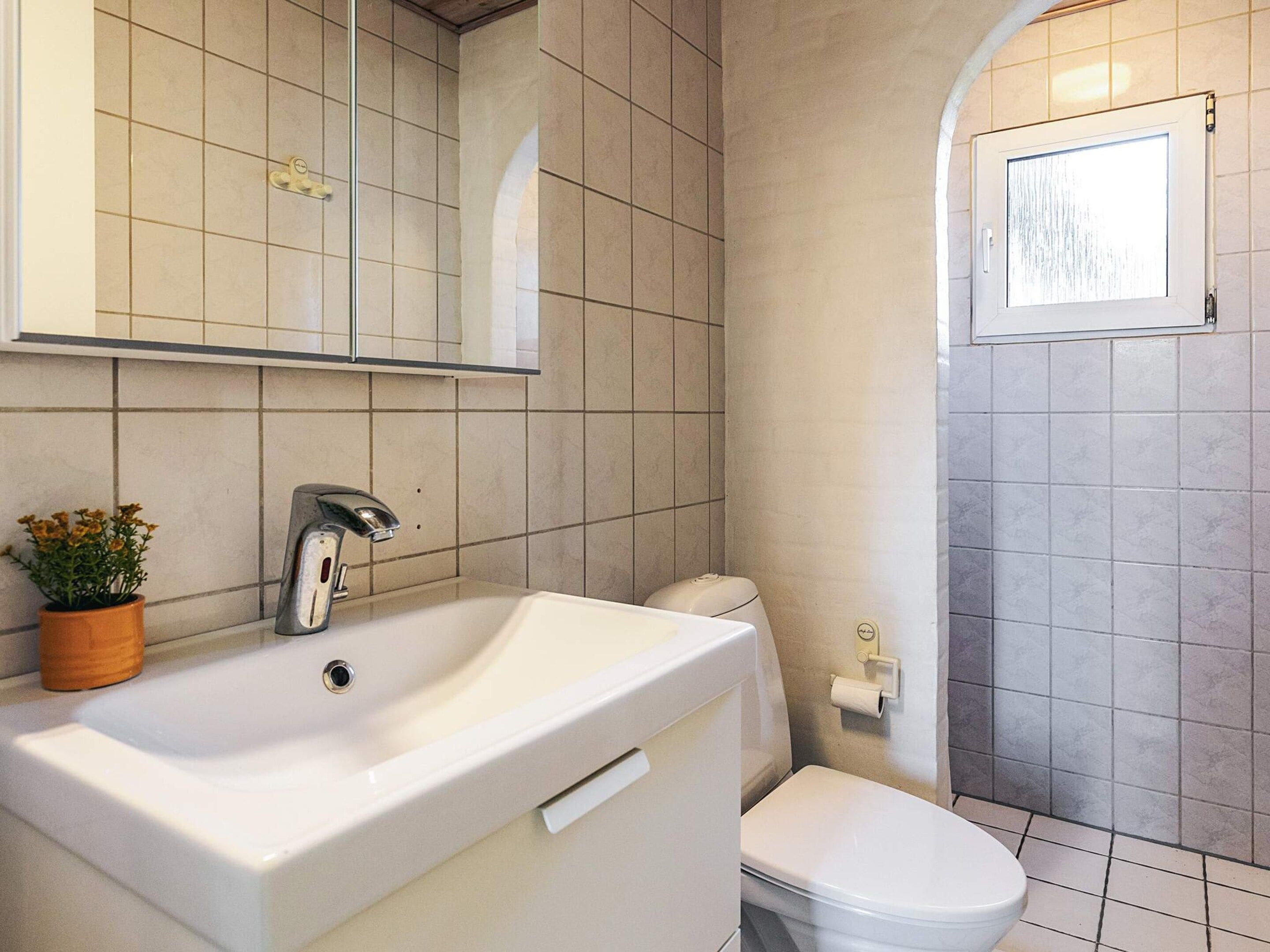 A bathroom with a white sink, a mirror, a toilet, and a window.