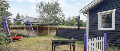 A backyard with a swing set, a bench, and a fenced area.
