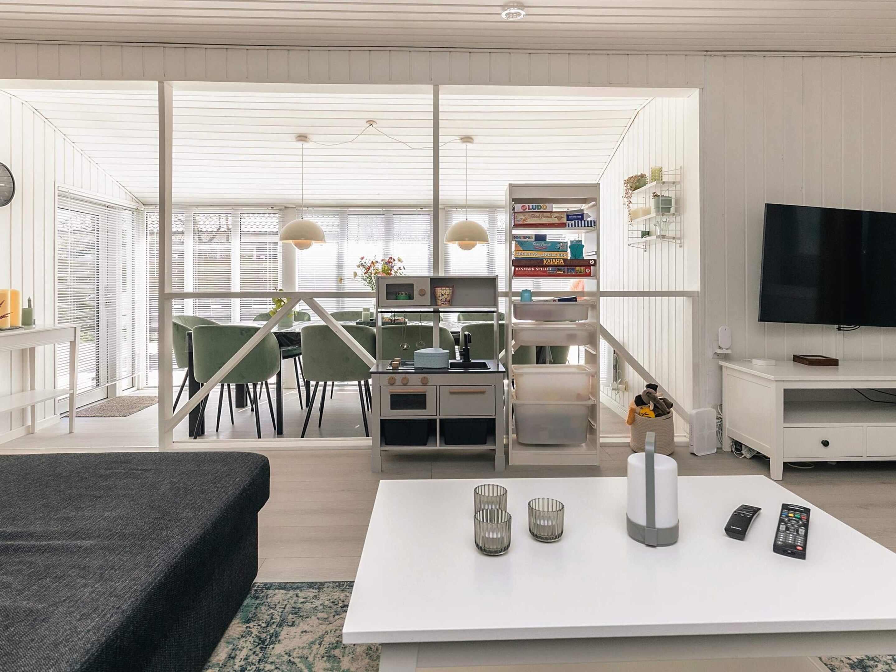 Una sala de estar moderna con un televisor de pantalla plana, una zona de comedor con sillas verdes y una cocina con estufa y armarios.
