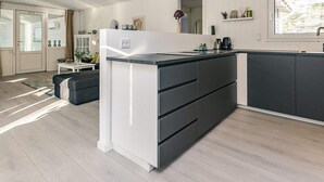 A modern kitchen with a central island, white cabinetry, and a large window providing natural light. - 4 Star Holiday Home in Vaeggerlose (Vaeggerlose)