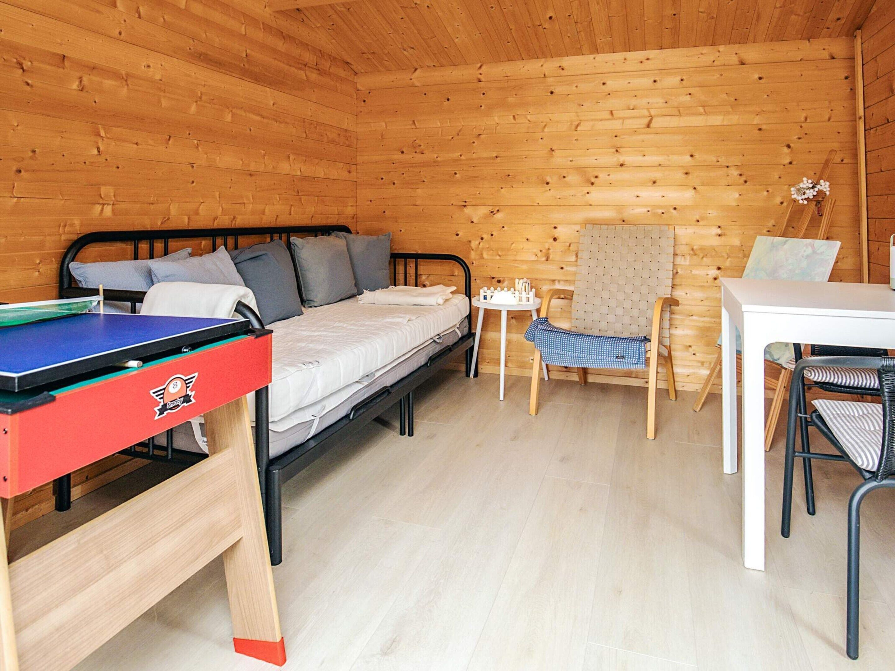 A compact room with a bed, a small table, a chair, and a ping pong table.