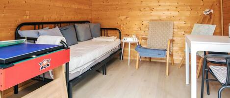 A compact room with a bed, a small table, a chair, and a ping pong table.
