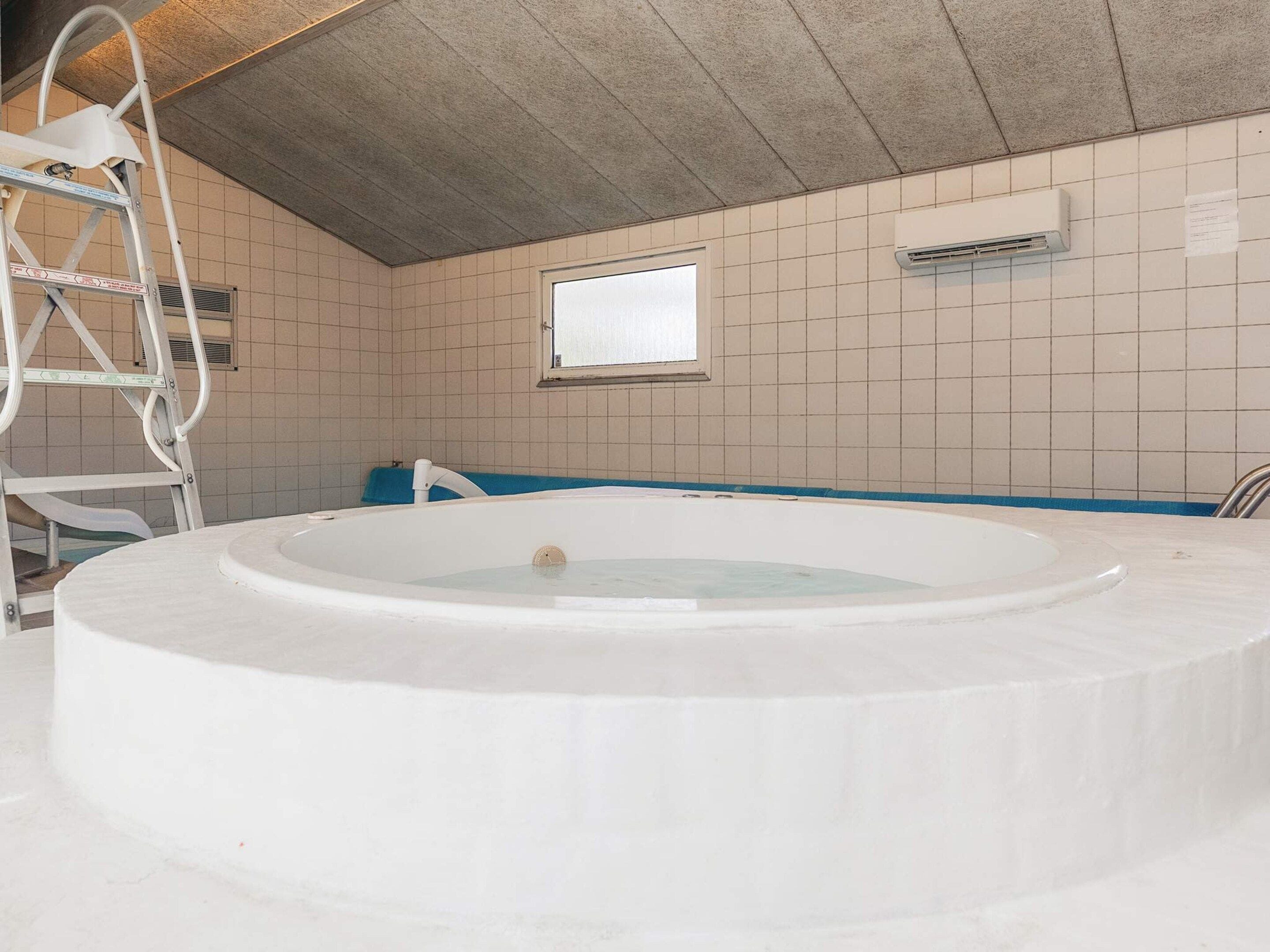 Une pièce avec une grande baignoire ronde, une fenêtre et une échelle.