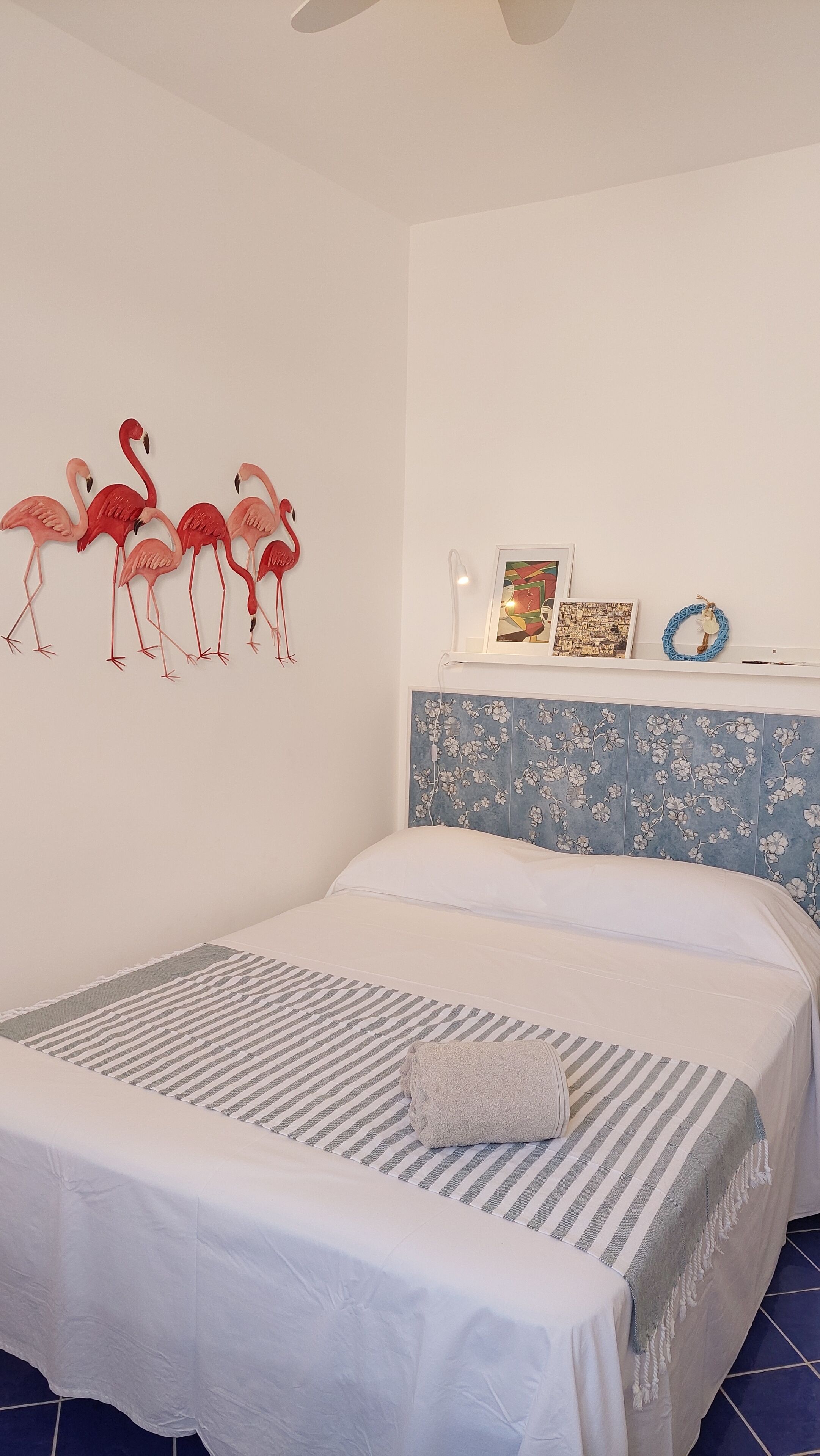A bedroom with a bed, a wall-mounted shelf with decorative items, and a ceiling fan.