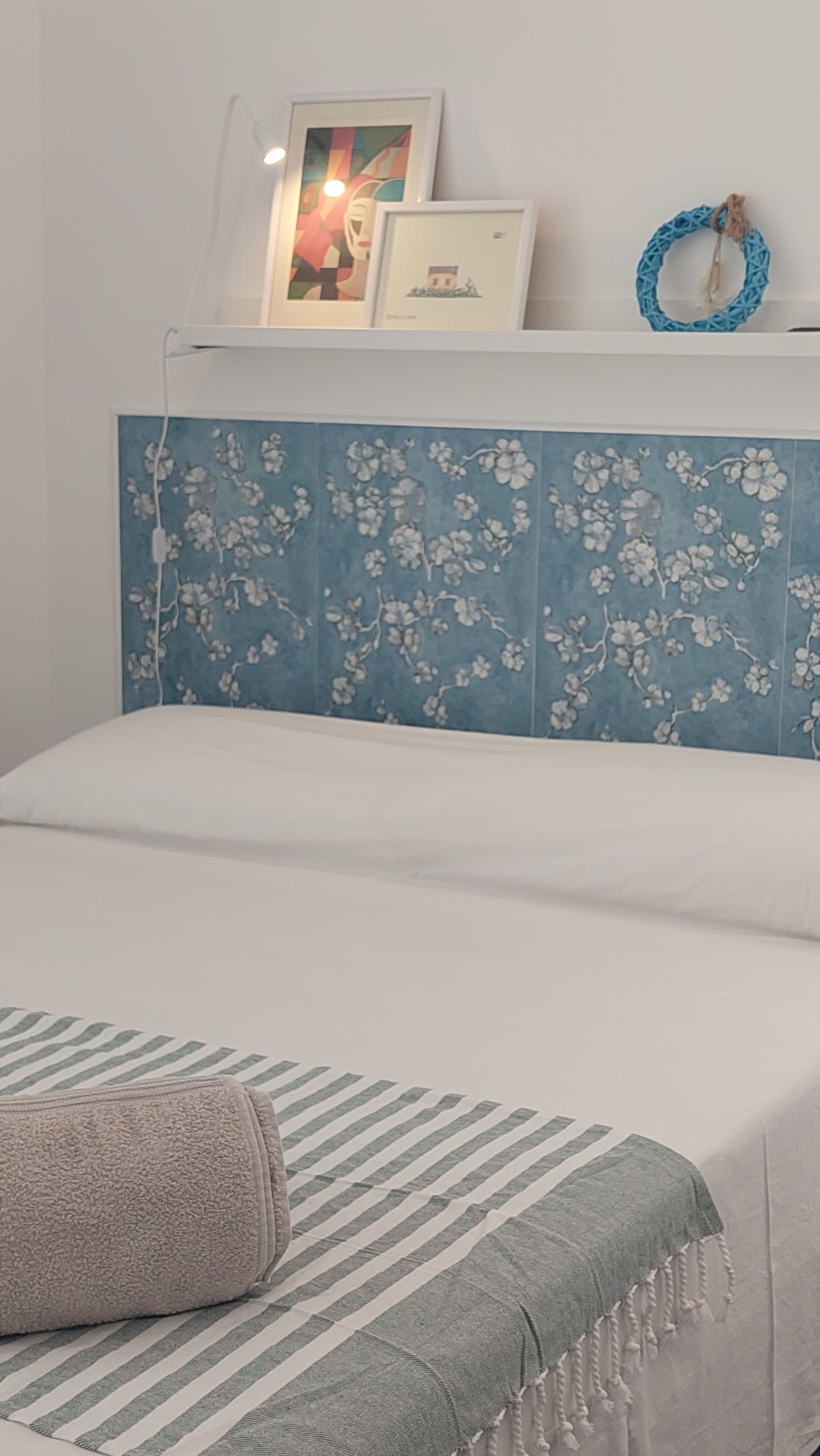 Een slaapkamer met een bed, een blauw bloemendecor op het hoofdeinde, een gestreept kussen en een blauwe muur.