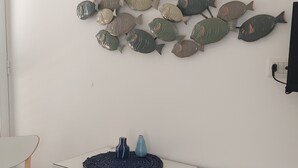 A room with a white desk, two chairs, a wall-mounted shelf with decorative fish, and a tiled floor. - AB Apartment (Ragusa)