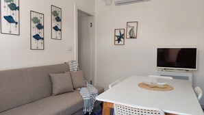 A living room with a sofa, a TV, and wall art. - AB Apartment (Ragusa)