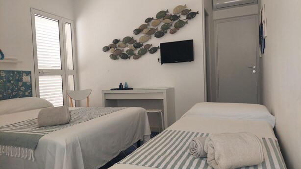 A hotel room with two beds, a desk, a TV, and a decorative fish wall art. - AB Apartment (Ragusa)