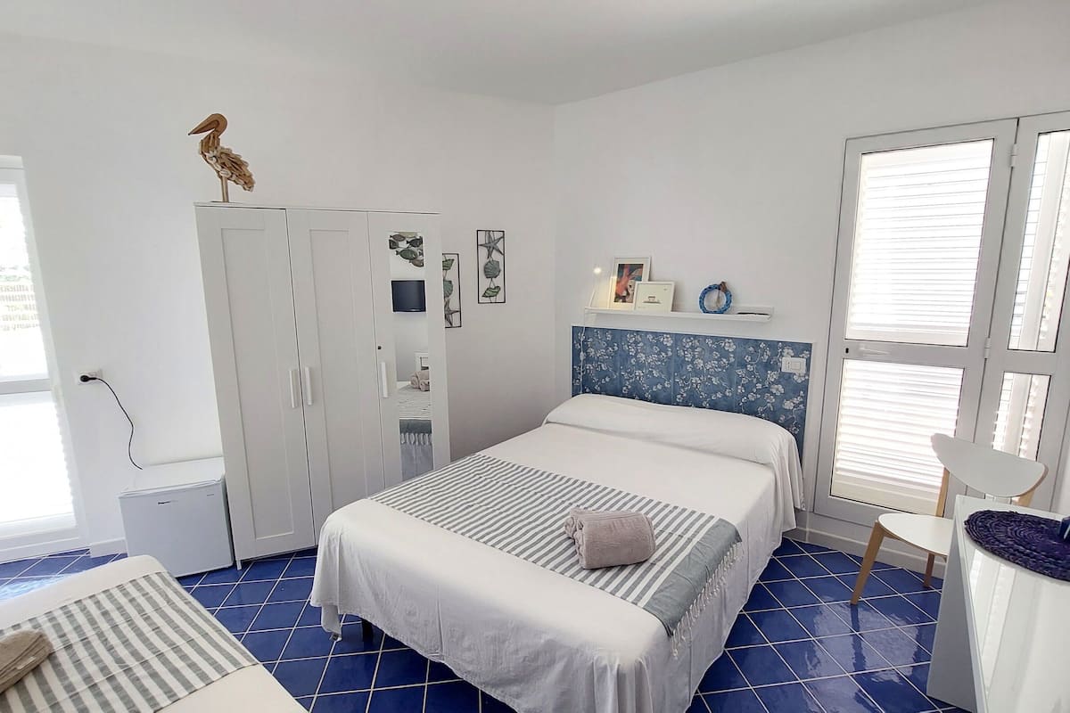 A bedroom with a bed, a wardrobe, a desk, and a window with blinds.