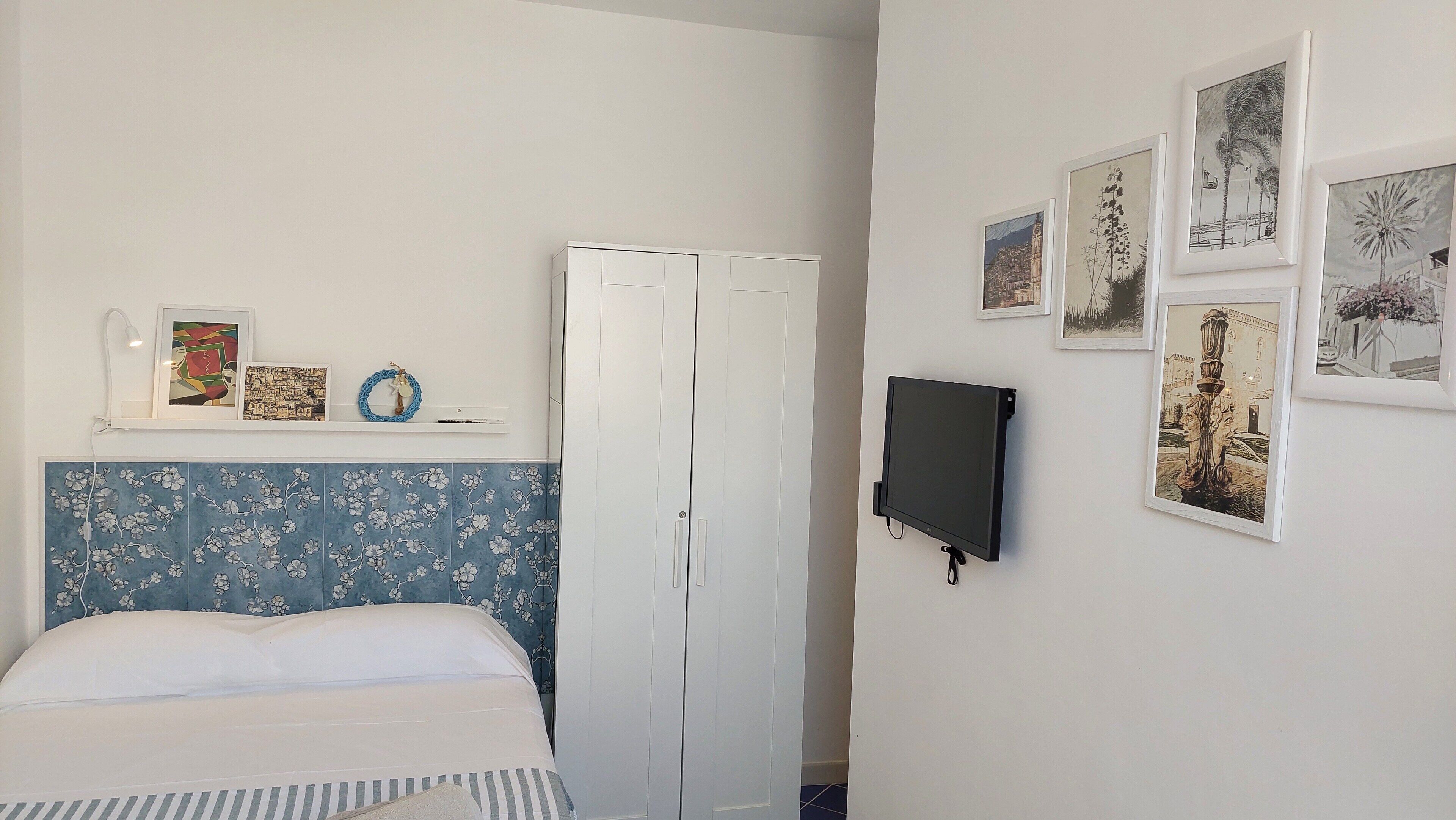 A bedroom with a bed, a wardrobe, and a wall-mounted TV.