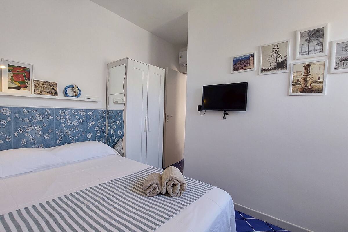 A bedroom with a bed, a TV, and artwork on the wall.