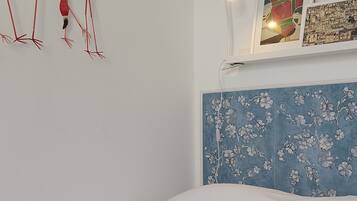 Quarto com cama, prateleira na parede com duas fotos emolduradas e decoração de flamingos.