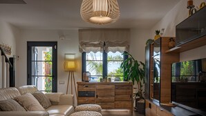 A modern living room with a sofa, ottomans, a coffee table, a TV, and a large window with curtains.