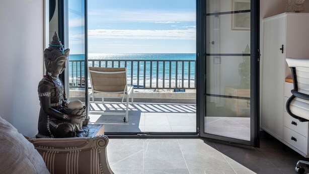 A room with a view of the sea, a statue, a chair, and a cabinet.