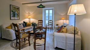 A cozy living room with two sofas, a wooden dining table, and chairs. There are lamps on either side of the room, and a window with a view outside. - Renovated country chic cottage, 6 bedrooms for 13, garden, terrace, Haute-Loire (Siaugues-Sainte-Marie)