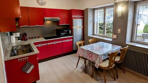 A compact kitchen with red cabinets, a dining table with chairs, a clock, and a window with a view.