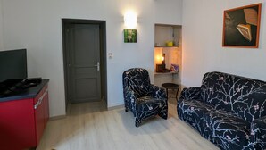 A living room with a sofa, two armchairs, a TV, and a red cabinet.