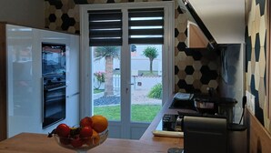A kitchen with a built-in oven, a microwave, and a coffee maker. There is a window with a view of a garden and a palm tree. - Family cottage with heated pool in Bretignolles-sur-Mer (Bretignolles-sur-Mer)