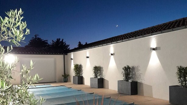 A swimming pool with a tiled deck, surrounded by potted plants and a white wall with exterior lighting. - Family cottage with heated pool in Bretignolles-sur-Mer (Bretignolles-sur-Mer)