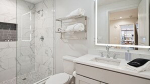 Un baño moderno con ducha de vidrio, inodoro blanco y tocador con espejo.