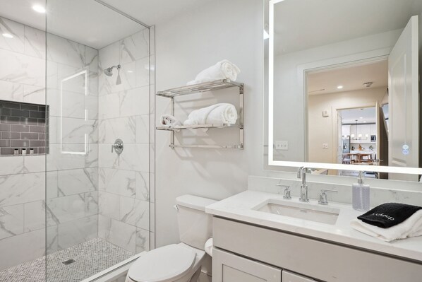 A modern bathroom with a glass-enclosed shower, a white toilet, and a vanity with a mirror.