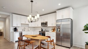 Una cocina moderna con armarios blancos, electrodomésticos de acero inoxidable y una mesa de comedor de madera con sillas.