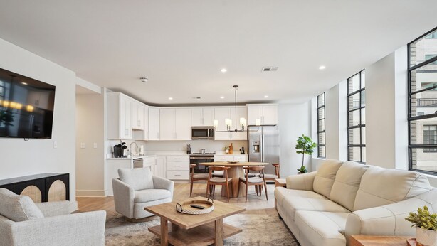 Una sala de estar moderna con sofá, sillón, mesa de centro y una zona de comedor con mesa y sillas.