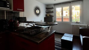 A compact kitchen with a central island, a microwave, and a red cabinet. A large mirror hangs on the wall, and a window provides a view of the outside. - Bright T2 with garage and WiFi in Aix-les-Bains (Aix-les-Bains)