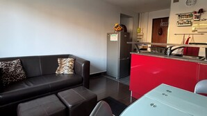 A modern living room with a black leather sofa, a red kitchen counter, and a stainless steel refrigerator. - Bright T2 with garage and WiFi in Aix-les-Bains (Aix-les-Bains)