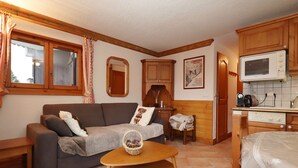 A cozy living room with a sofa, a small wooden table, and a kitchen area with wooden cabinets and a microwave. - 2-room cabin apartment in Les Houches, 6 guests, pets welcome (Les Houches)