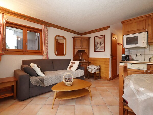 Un salon chaleureux avec un canapé, une petite table en bois et un coin cuisine doté de meubles en bois et d’un four à micro-ondes.