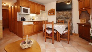 A compact kitchen with wooden cabinets, a microwave, a stone wall, and a dining area with a table and chairs. - 2-room cabin apartment in Les Houches, 6 guests, pets welcome (Les Houches)