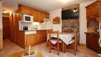 A compact kitchen with wooden cabinets, a microwave, a stone wall, and a dining area with a table and chairs.