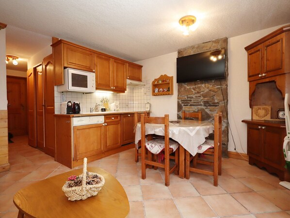 Une cuisine compacte avec des meubles en bois, un four à micro-ondes, un mur en pierre et un coin repas comprenant une table et des chaises.