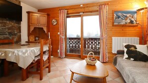 A cozy room with a wooden interior, a dining table with chairs, a sofa, and a window with curtains. - 2-room cabin apartment in Les Houches, 6 guests, pets welcome (Les Houches)