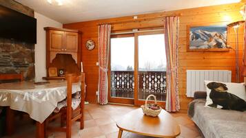 A cozy room with a wooden interior, a dining table with chairs, a sofa, and a window with curtains.
