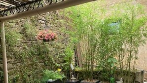 Een overdekt terras met een stenen muur, potplanten en een zithoek.