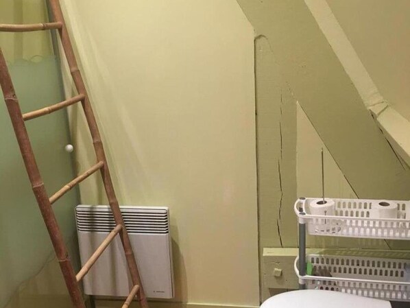 Una habitación con un radiador blanco, una escalera de bambú y una cesta de plástico blanca.
