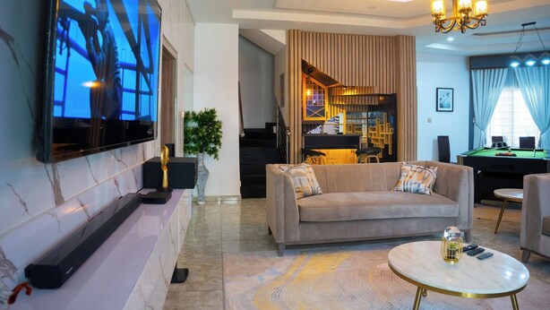 A modern living room with a flat-screen TV, a beige sofa, a round coffee table, and a pool table. - Uphoria Apartments (Abuja)