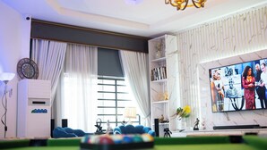 A modern living room with a large TV, comfortable seating, and a decorative chandelier. - Uphoria Apartments (Abuja)
