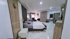 A modern hotel room with a large bed, a bedside table, a wardrobe, and a seating area with a chair and a small table. - Uphoria Apartments (Abuja)