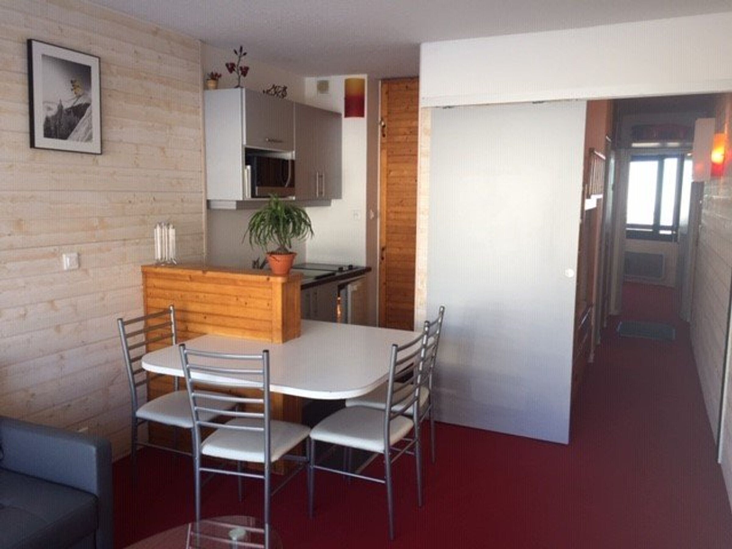 A compact room with a dining table and chairs, a small kitchen area with cabinets and a microwave, and a potted plant.