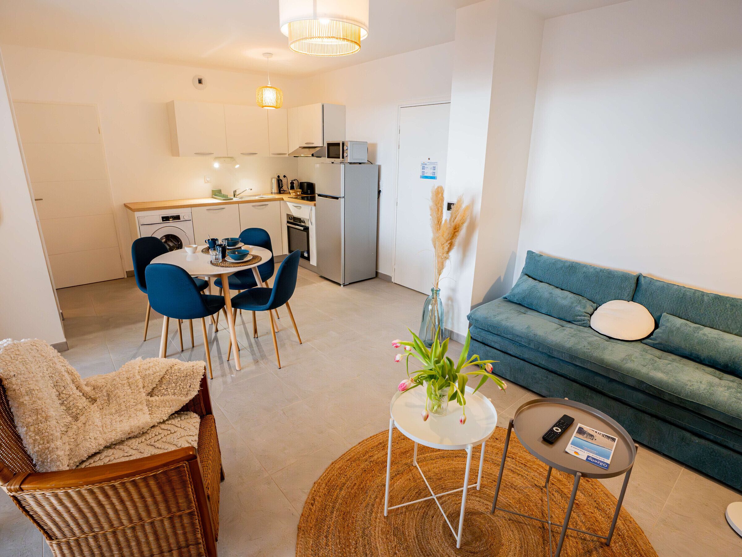 Un salon moderne comprenant un canapé, une table à manger avec des chaises, un coin cuisine et une petite table d’appoint avec une télécommande.