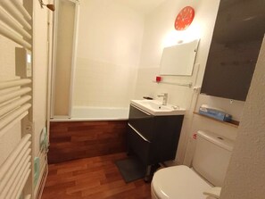 A small bathroom with a white toilet, a sink with a mirror above it, and a shower area. - Studio Cabin 6 Pax, Balcony Near Slopes, St Lary Soul. (Saint-Lary-Soulan)